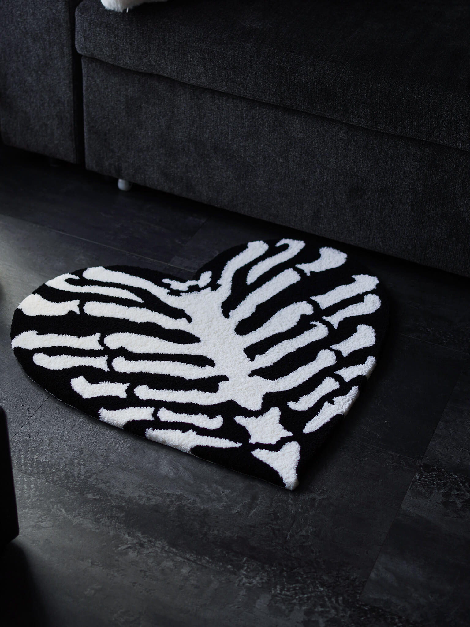 Ribcage Heart Rug placed next to a sofa on a concrete floor.