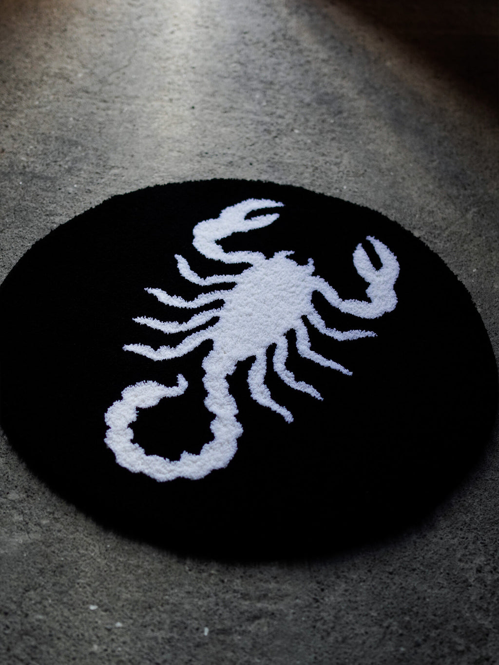 Angled lighting on the Scorpion rug, revealing the deep black canvas and raised white hand-stitching.